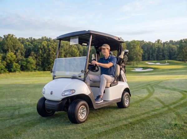 White electric golf cart on green golf course fairway at golden hour with golfer driving.